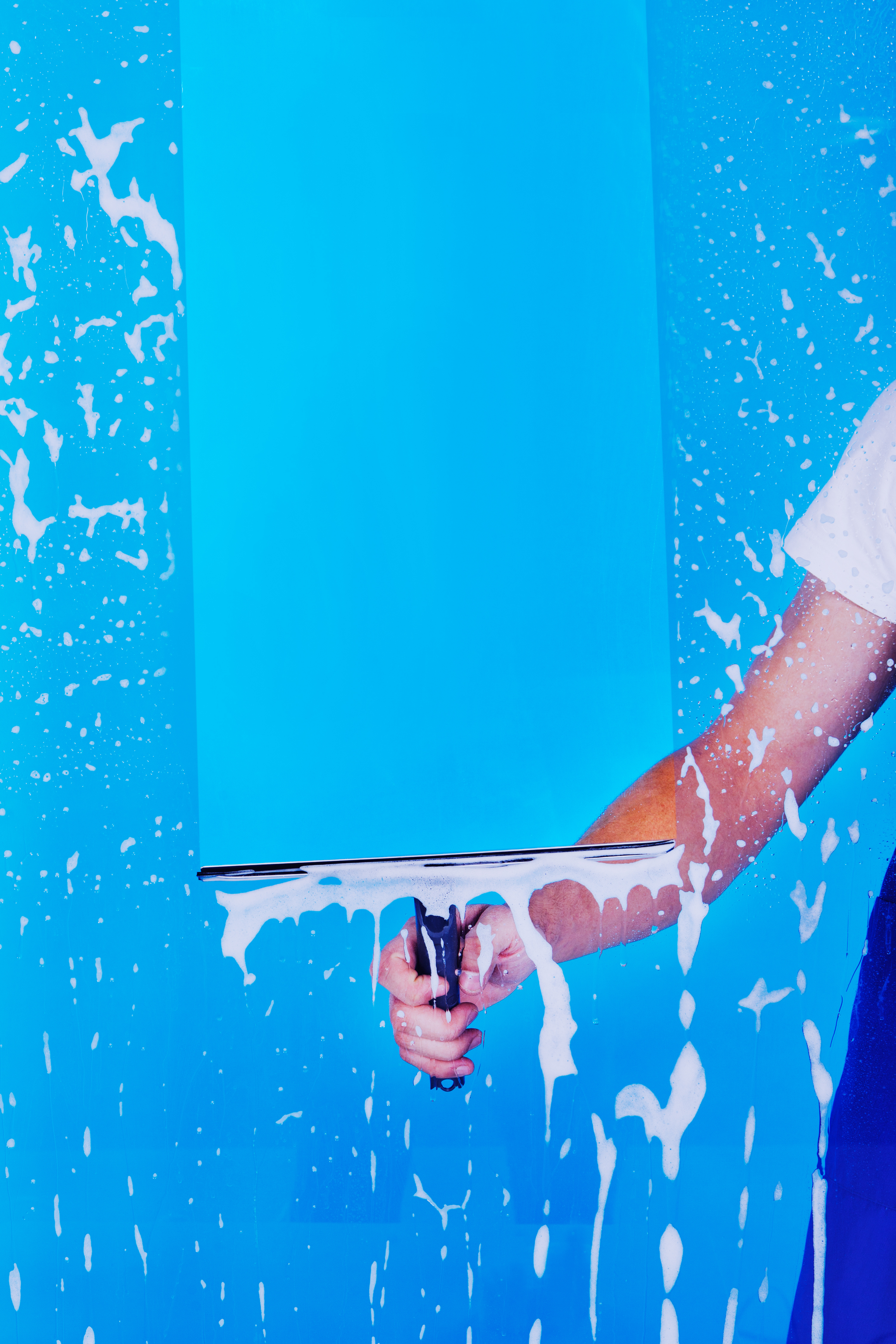 Cropped image male servant cleaning glass with squeegee over blue background