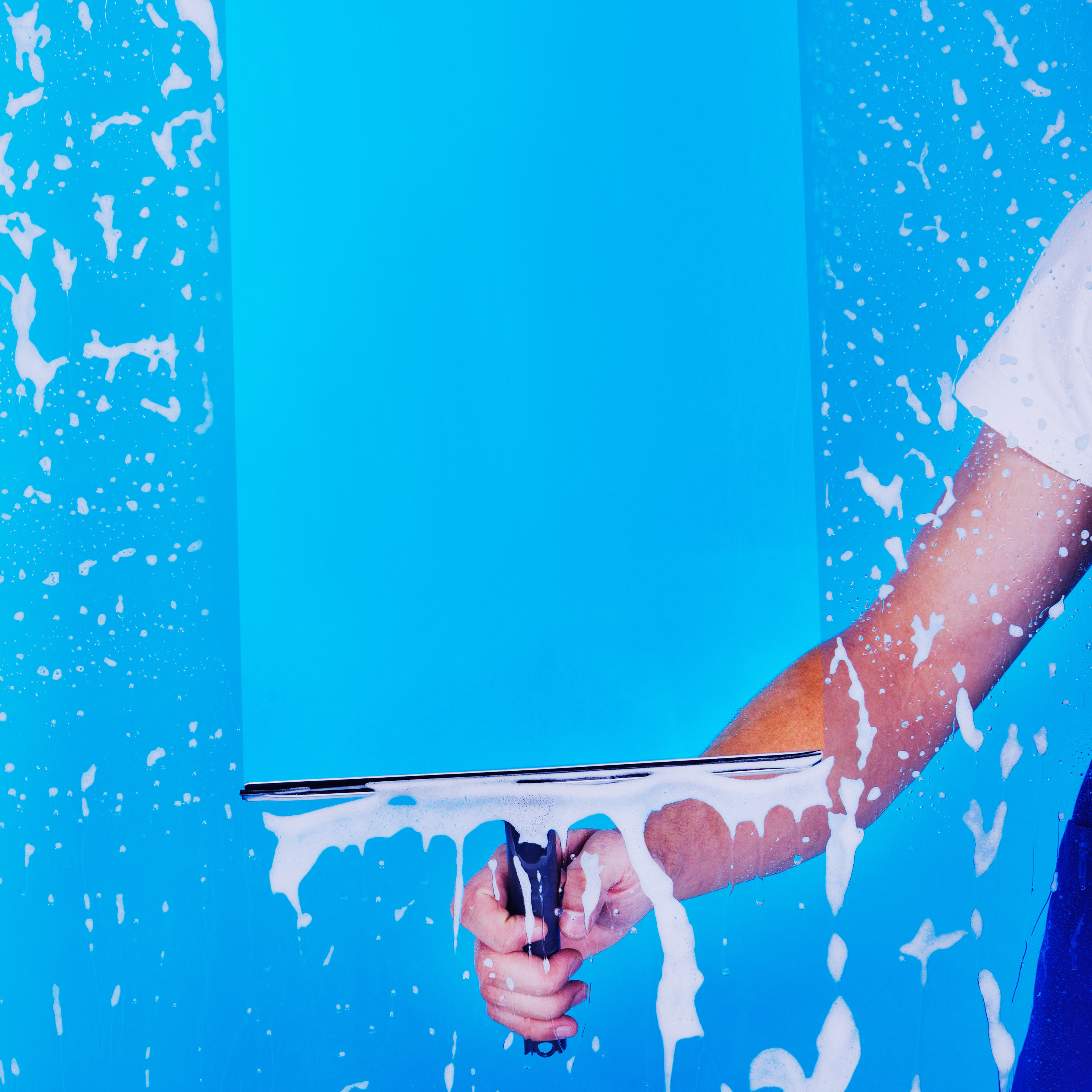 Cropped image male servant cleaning glass with squeegee over blue background